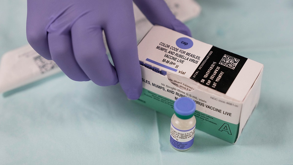 A box of the MMR vaccine, the foreground of the guided hand box of the MMR vaccine next to a vaccine road.
