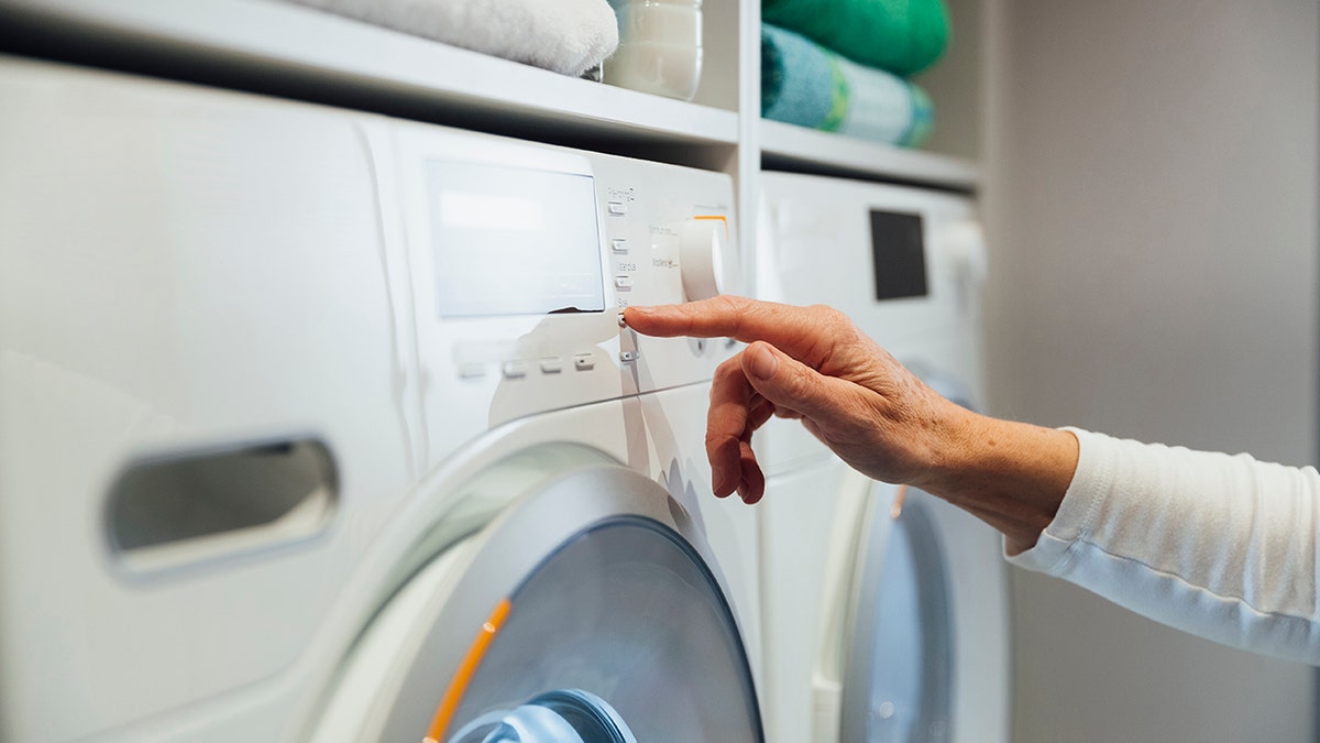 Person pressing the buttons in a washing machine. Only the hand is visible, shot from the side.
