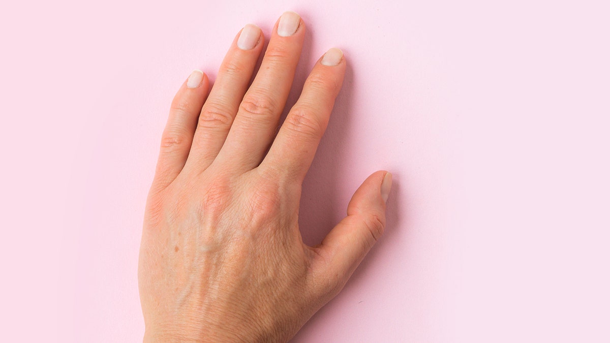 Image of the left hand nearby, putting palm on a pink background. The nails are careful and painted in a light pink.