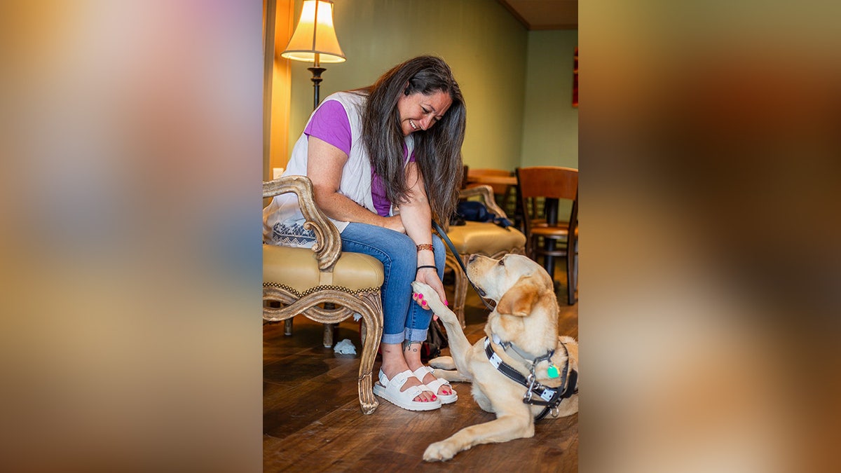 A woman smiles while receiving a shake from her dog's guy's paw in a warm room