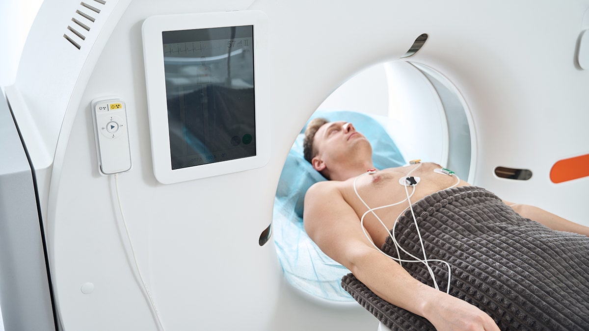 Adult male with ECG electrodes placed on the chest located in supine position within the opening of the CT CT